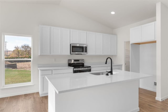 kitchen with light countertops, vaulted ceiling, a sink, white cabinets, and appliances with stainless steel finishes