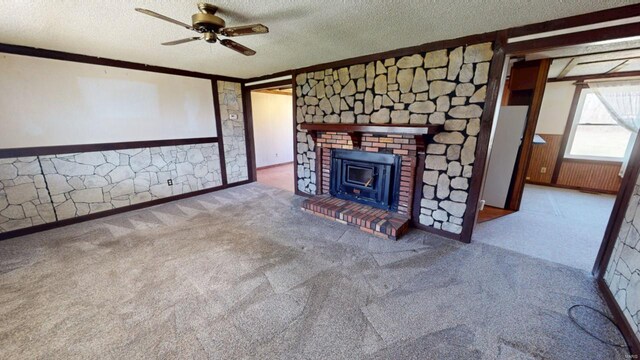 unfurnished living room with a textured ceiling, ornamental molding, ceiling fan, and a wainscoted wall