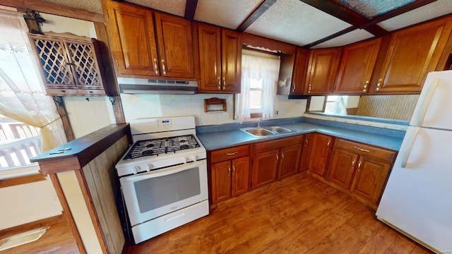kitchen with brown cabinetry, white appliances, light wood-type flooring, under cabinet range hood, and a sink