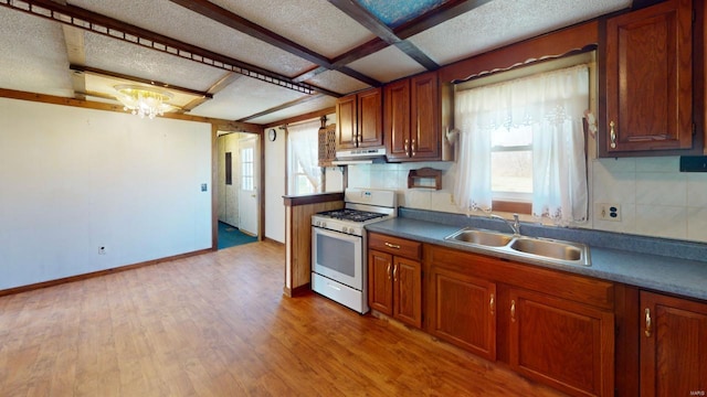kitchen featuring a sink, brown cabinets, under cabinet range hood, and white range with gas cooktop