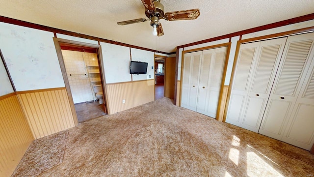 unfurnished bedroom featuring wainscoting, ensuite bath, a textured ceiling, carpet, and two closets