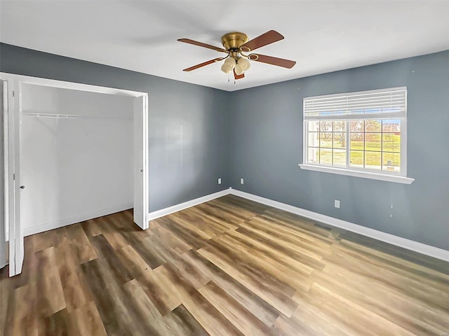 unfurnished bedroom with baseboards, wood finished floors, a closet, and a ceiling fan