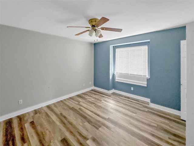 unfurnished room featuring baseboards, visible vents, wood finished floors, and a ceiling fan