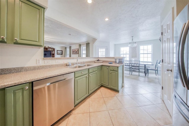 kitchen with a peninsula, stainless steel appliances, a sink, green cabinetry, and light tile patterned floors