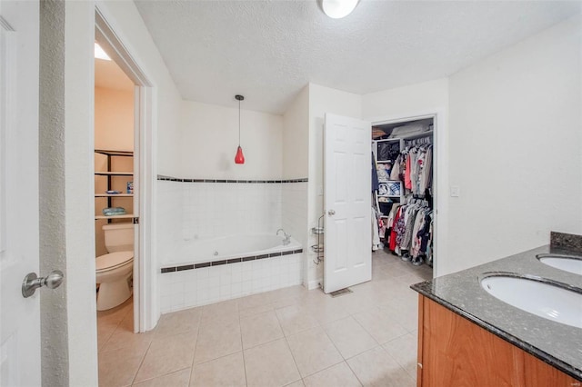 bathroom with toilet, a sink, a relaxing tiled tub, a spacious closet, and a textured ceiling