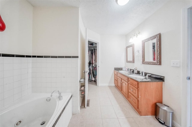 bathroom with a textured ceiling, double vanity, a sink, tile patterned flooring, and a whirlpool tub