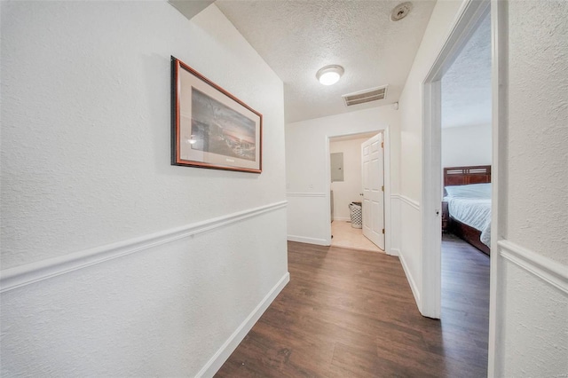 hall featuring wood finished floors, a textured wall, a textured ceiling, and visible vents