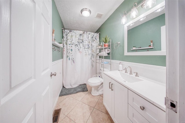 bathroom featuring a wainscoted wall, visible vents, tile patterned flooring, and a textured ceiling