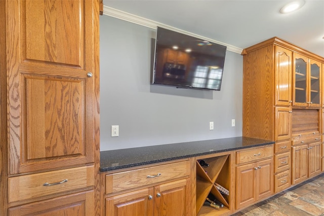 kitchen featuring dark stone counters, ornamental molding, stone finish flooring, and glass insert cabinets