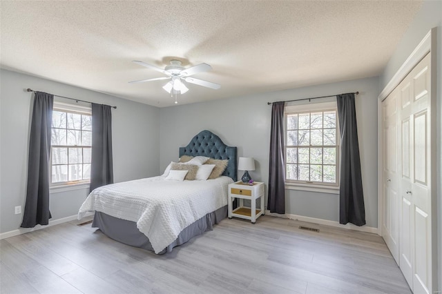 bedroom with light wood-type flooring, a closet, multiple windows, and visible vents