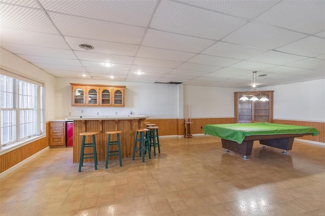 playroom featuring a drop ceiling, wet bar, wooden walls, and wainscoting