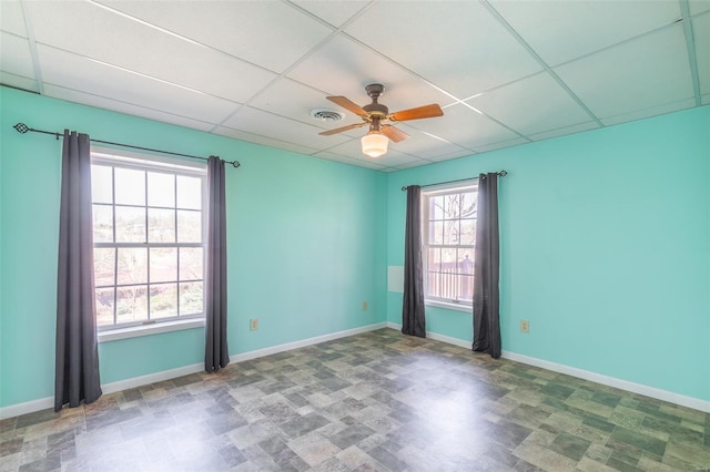 empty room with baseboards, visible vents, a drop ceiling, and a ceiling fan