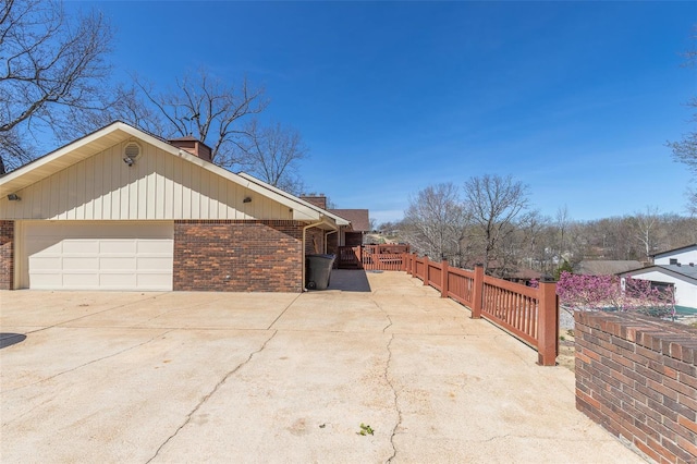 view of side of home featuring a chimney, fence, brick siding, and concrete driveway