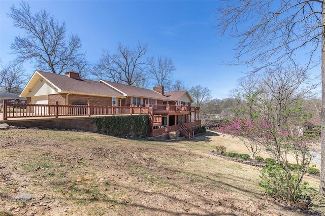 back of property with a wooden deck, brick siding, a yard, and a chimney