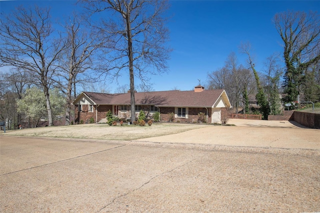 ranch-style home featuring a chimney, brick siding, and concrete driveway