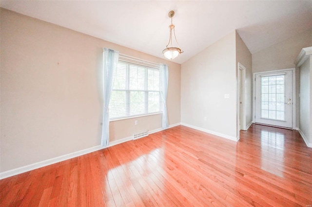 empty room featuring baseboards, vaulted ceiling, light wood-type flooring, and visible vents