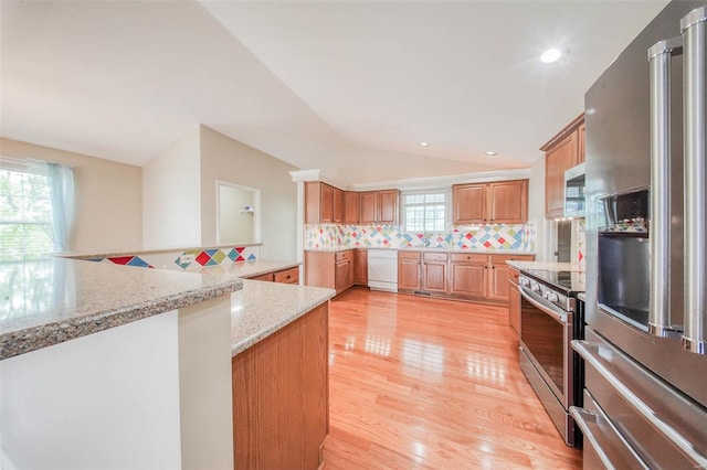 kitchen featuring appliances with stainless steel finishes, light stone counters, light wood-style floors, lofted ceiling, and tasteful backsplash