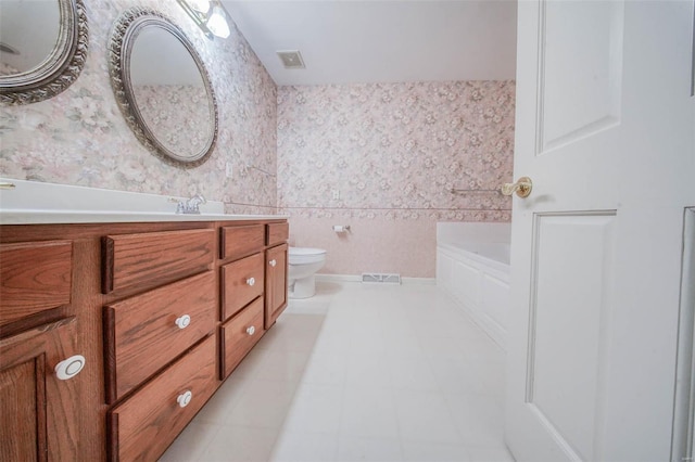 bathroom featuring a bath, wainscoting, vanity, toilet, and wallpapered walls