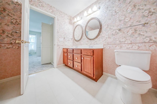 bathroom with double vanity, toilet, wallpapered walls, and a sink