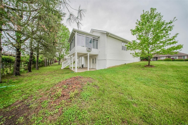 rear view of property featuring a lawn, stairs, a sunroom, and a patio area