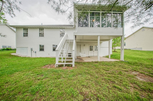 rear view of property featuring a lawn, a sunroom, stairway, and a patio area