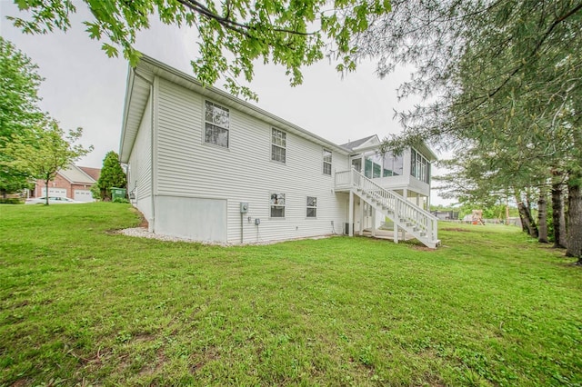 back of house featuring a lawn, a sunroom, and stairway