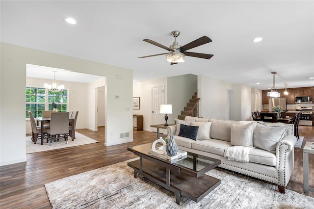 living room featuring stairs, wood finished floors, baseboards, recessed lighting, and ceiling fan with notable chandelier