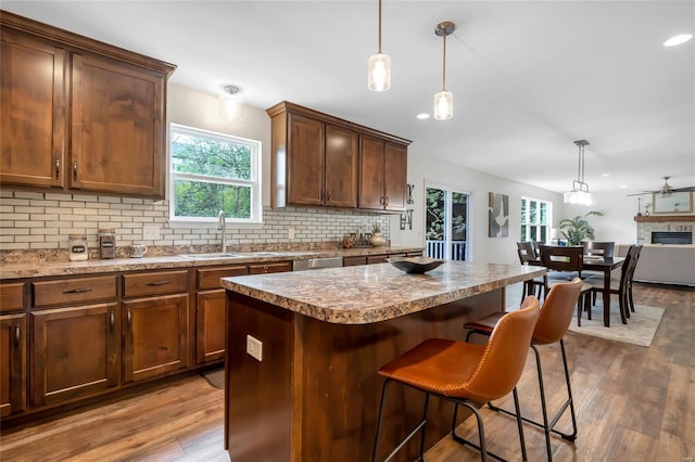 kitchen featuring wood finished floors, a breakfast bar area, a sink, backsplash, and decorative light fixtures