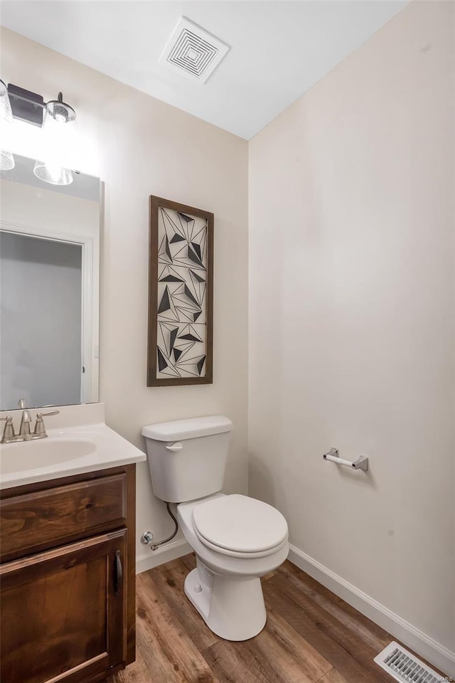 half bath featuring toilet, visible vents, wood finished floors, and vanity