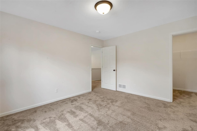 unfurnished bedroom featuring a walk in closet, visible vents, baseboards, a closet, and carpet
