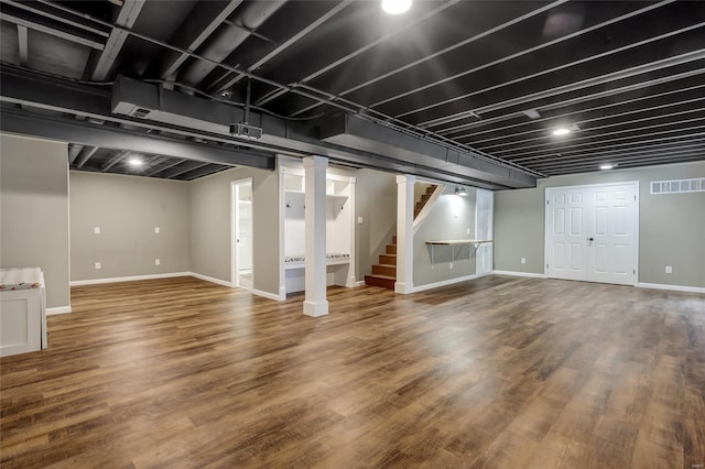 finished below grade area featuring baseboards, wood finished floors, visible vents, and stairway