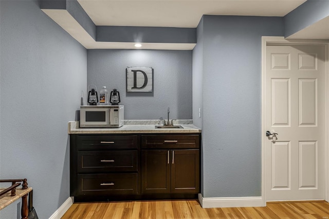bar featuring baseboards, white microwave, a sink, and light wood-type flooring