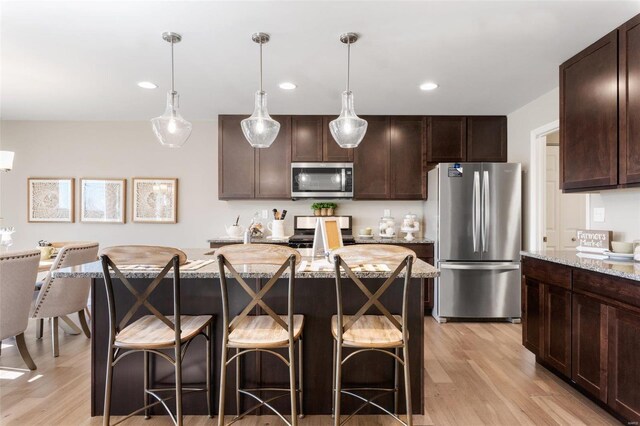 kitchen with light stone counters, appliances with stainless steel finishes, a center island, light wood-style floors, and dark brown cabinets