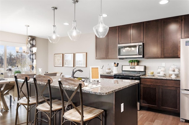 kitchen with light wood-style flooring, light stone countertops, a kitchen island with sink, stainless steel appliances, and a breakfast bar area