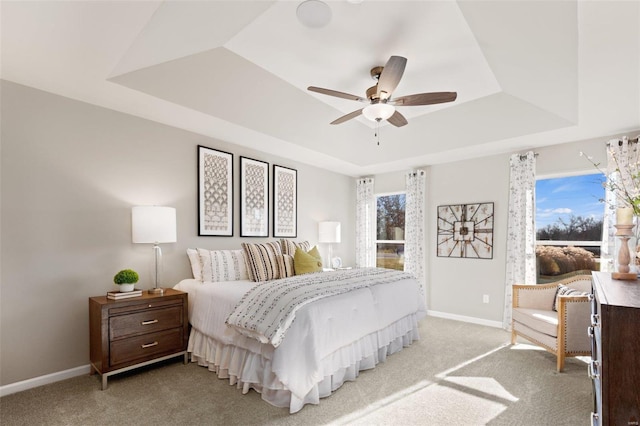 bedroom featuring a tray ceiling, baseboards, light carpet, and a ceiling fan