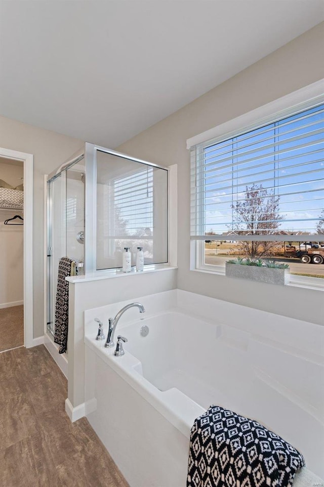 full bath with a garden tub, a shower stall, wood finished floors, a walk in closet, and baseboards