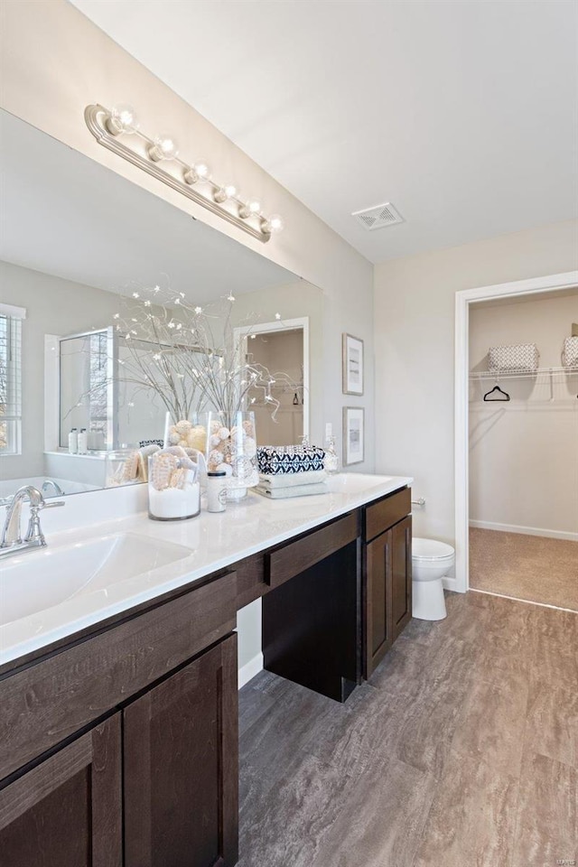 full bathroom featuring visible vents, double vanity, toilet, a sink, and a walk in closet