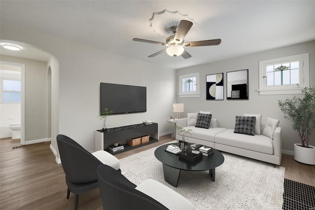 living area with baseboards, arched walkways, wood finished floors, and a ceiling fan