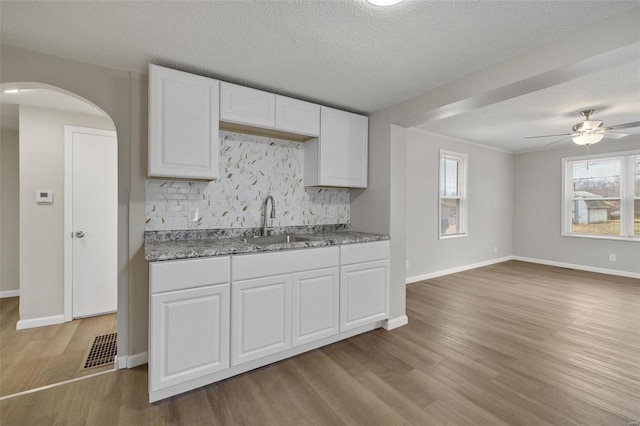 kitchen with backsplash, a sink, wood finished floors, white cabinets, and arched walkways