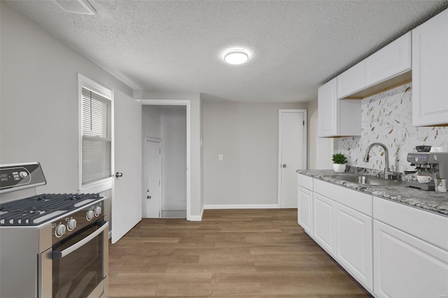 kitchen with white cabinetry, stainless steel gas range oven, a sink, light wood finished floors, and visible vents