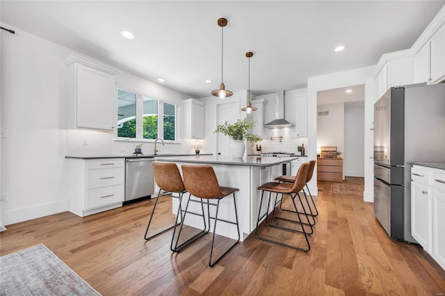 kitchen with light wood-style floors, wall chimney exhaust hood, a sink, stainless steel appliances, and a breakfast bar area