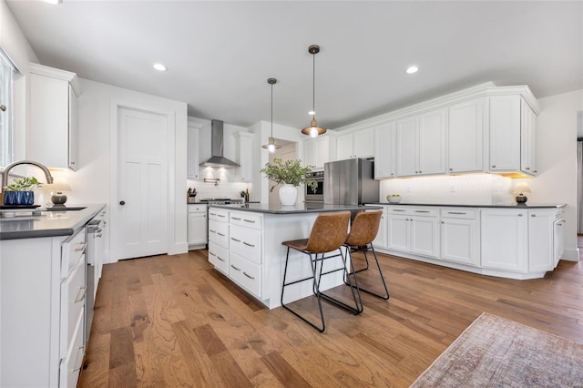 kitchen featuring tasteful backsplash, wall chimney exhaust hood, a sink, dark countertops, and stainless steel appliances