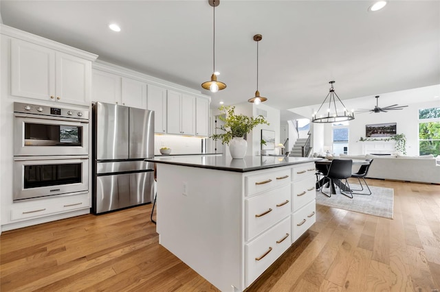 kitchen with white cabinets, a center island, open floor plan, dark countertops, and stainless steel appliances