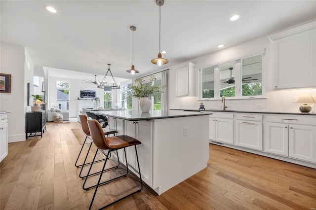 kitchen with dark countertops, light wood-style floors, a breakfast bar area, ceiling fan with notable chandelier, and a sink