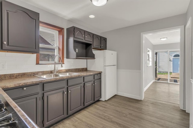 kitchen with a sink, decorative backsplash, freestanding refrigerator, and light wood-style floors