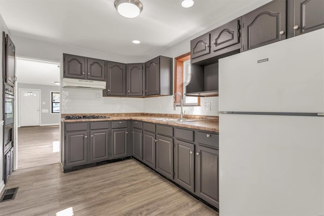kitchen featuring freestanding refrigerator, under cabinet range hood, visible vents, gas stovetop, and a sink