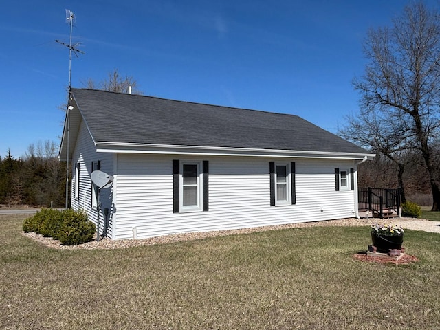 view of side of home with a shingled roof and a yard