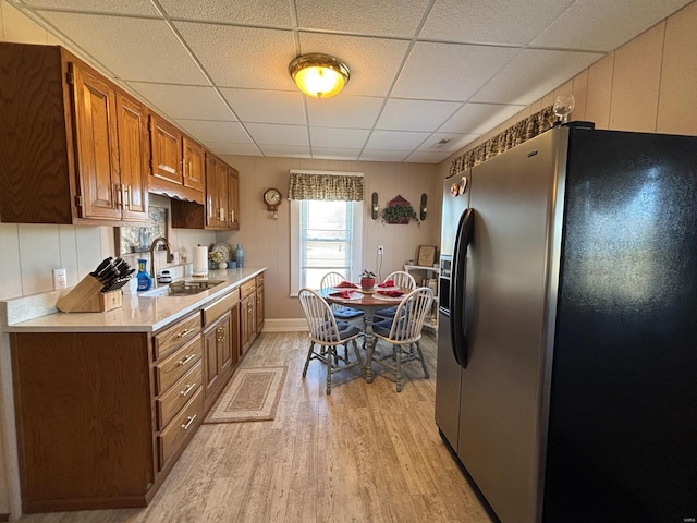 kitchen with light countertops, light wood finished floors, a sink, stainless steel refrigerator with ice dispenser, and a paneled ceiling