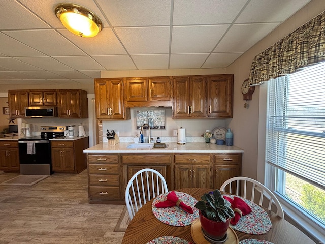 kitchen featuring light countertops, brown cabinetry, appliances with stainless steel finishes, a sink, and a paneled ceiling