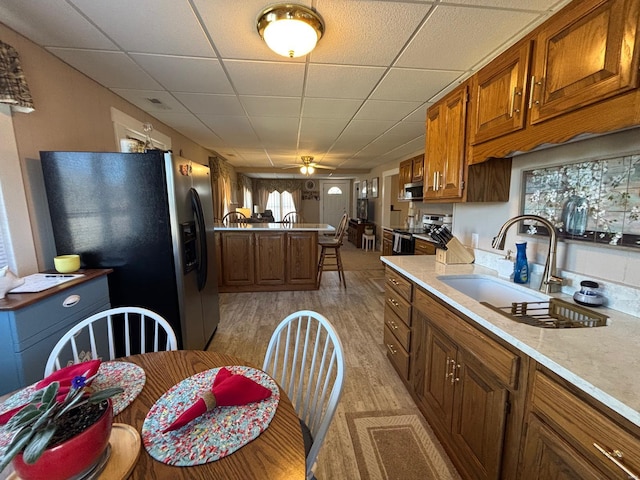 kitchen with light countertops, a sink, light wood finished floors, brown cabinetry, and stainless steel appliances